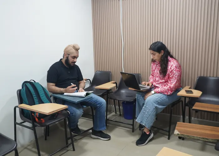 Two people seated with a notebook and laptop in a classroom