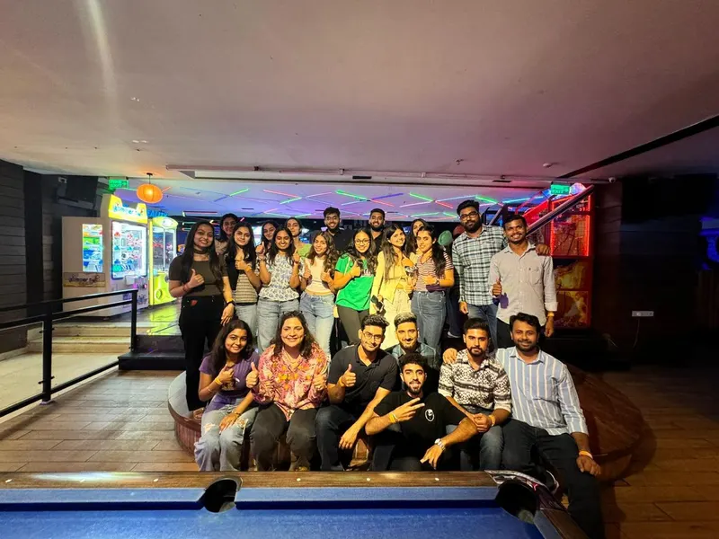 A group posing behind a pool table beside arcade games