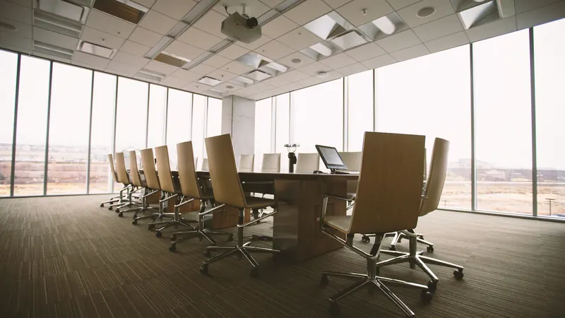 Empty conference room with wooden table and chairs beside tall windows