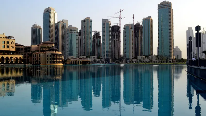Tall waterfront buildings reflected in calm blue water under clear skies