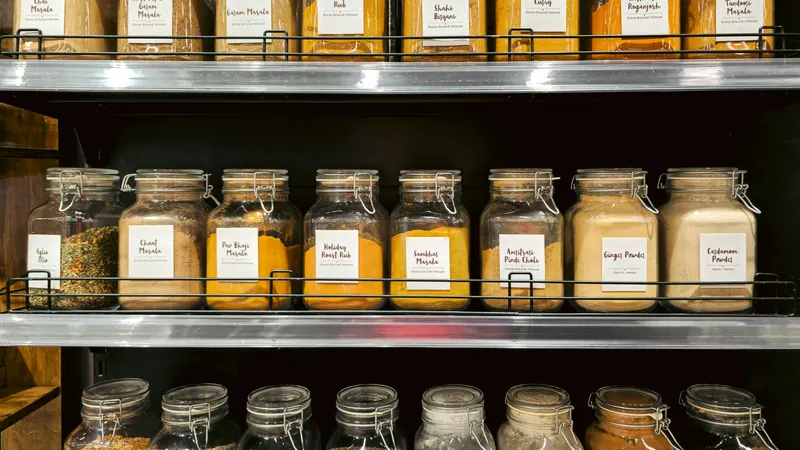 Glass jars containing colourful spices arranged on dark metal shelves