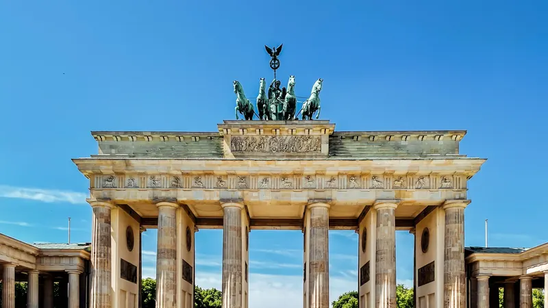 Stone gateway with columns and a rooftop sculpture beneath blue sky