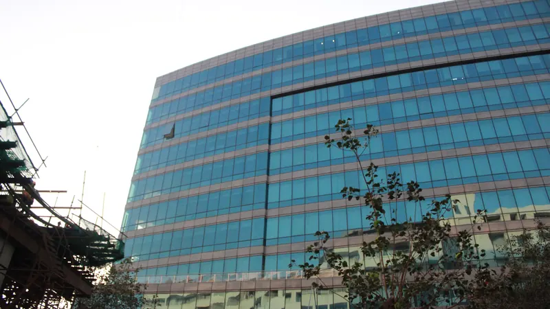 Glass fronted NMIMS building rising above trees beneath a cloudy sky