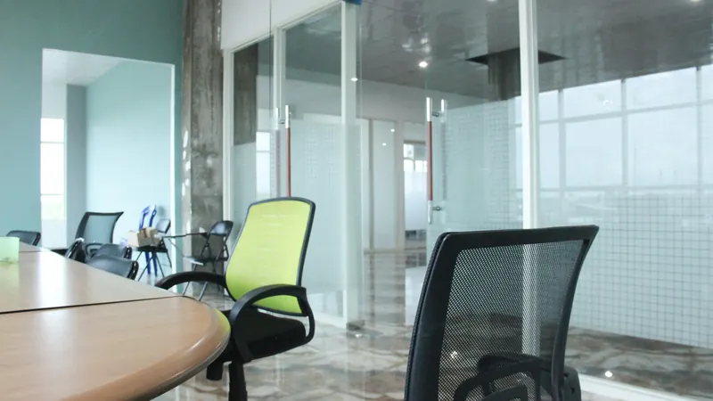 Green and dark chairs around a table beside office windows