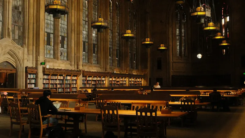 Library tables and lamps beside tall windows and wooden shelves