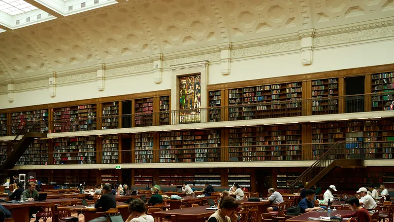 Library readers beneath an ornate ceiling beside tall wooden bookshelves