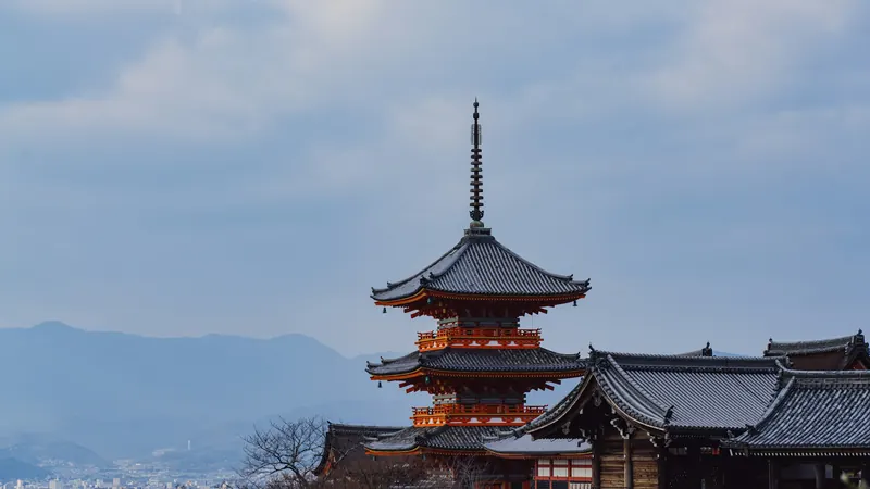 Japanese pagoda above rooftops with mountains beneath a cloudy sky