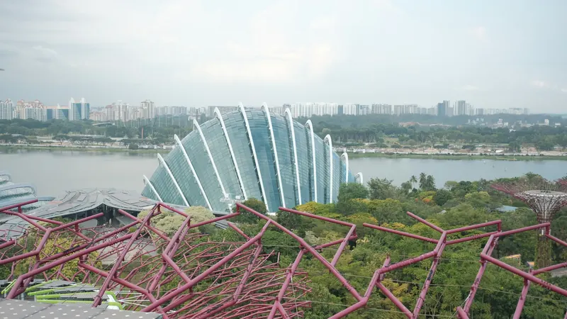 Curved glass structures and planted walkways overlooking water and distant buildings