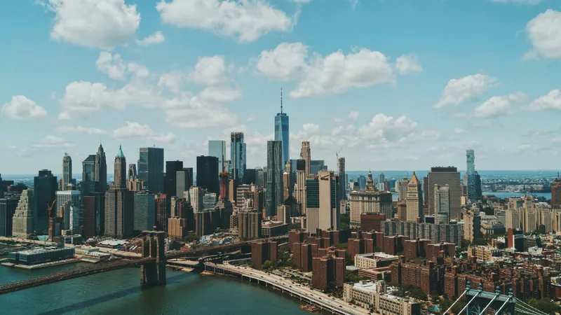 Dense waterfront city skyline with tall towers beneath scattered white clouds