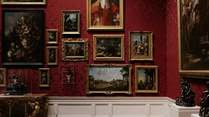 Framed paintings arranged closely together on a dark red gallery wall