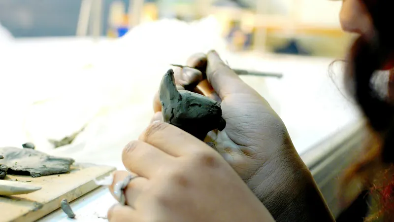 Hands shaping a small clay object at a work surface