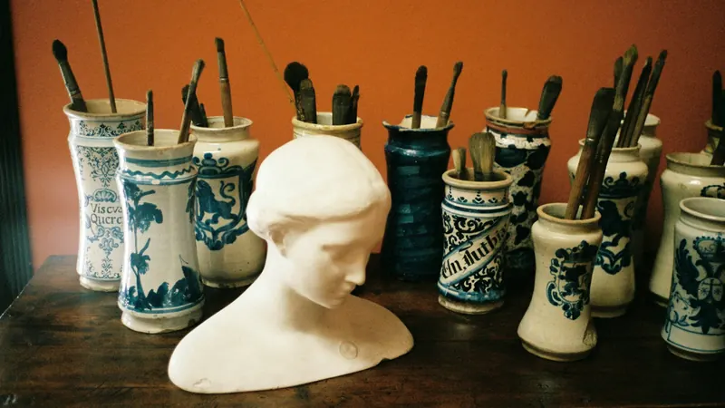 Paintbrushes in decorated containers beside a small white sculpted bust