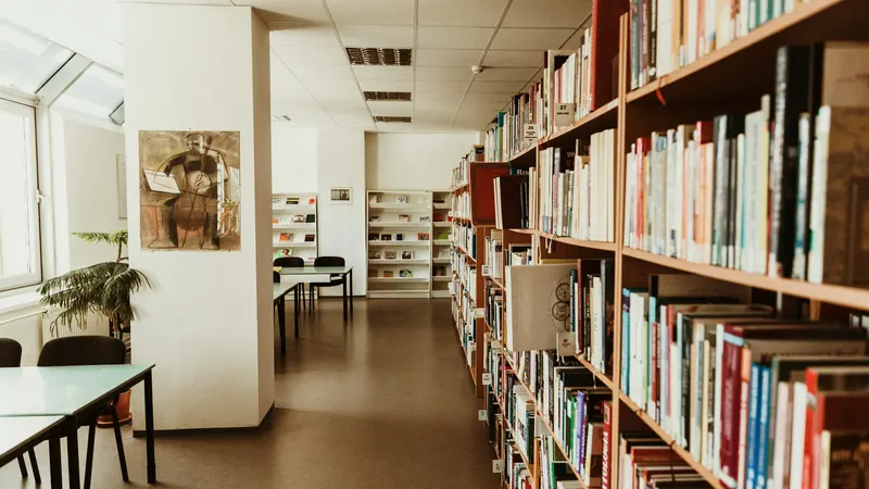 Library bookshelves beside study tables in a bright narrow room