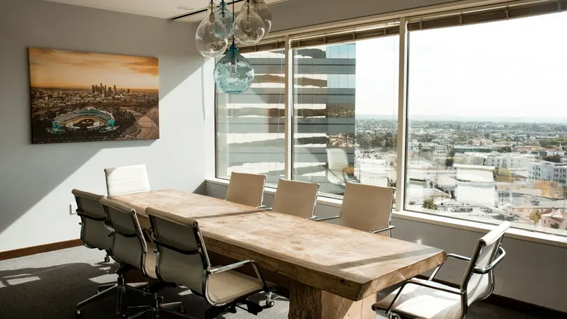 Wooden conference table and chairs beside windows overlooking city buildings