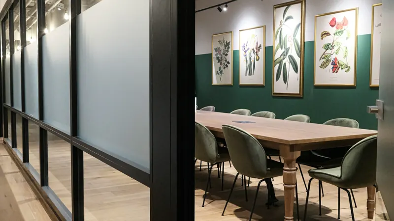 Wooden meeting table beneath botanical pictures in a glass enclosed room