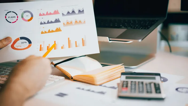 Hands reviewing printed financial charts beside a calculator and laptop