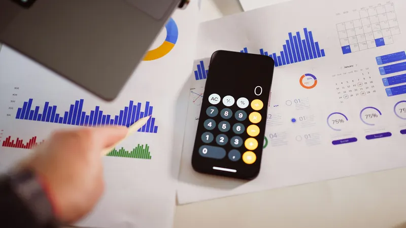 Phone calculator resting on printed charts beside a person's hand