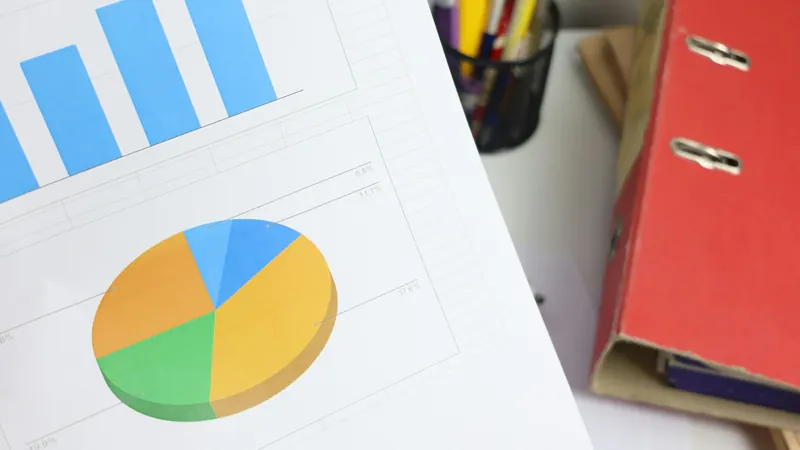 Printed bar charts and colourful pie chart beside stacked folders