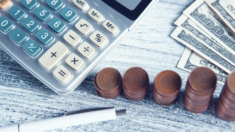 Calculator beside stacked coins and banknotes on a wooden surface