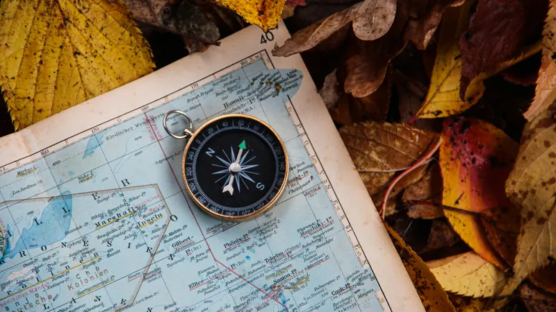 Round compass resting on a folded map beside fallen leaves