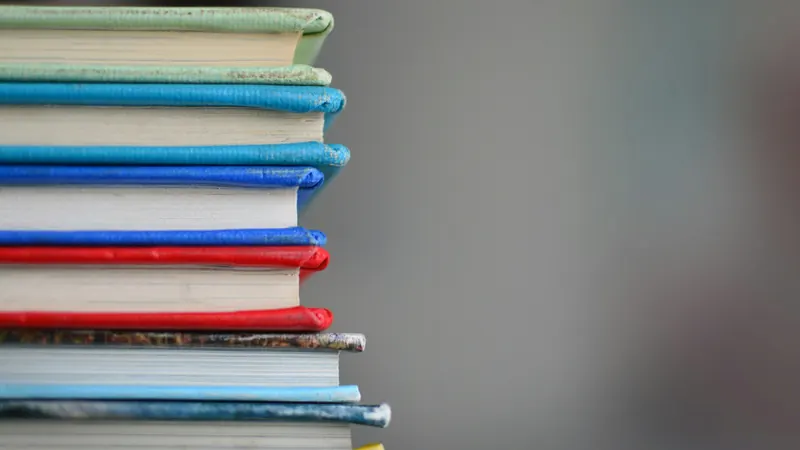 Stack of colourful closed books against a plain grey background