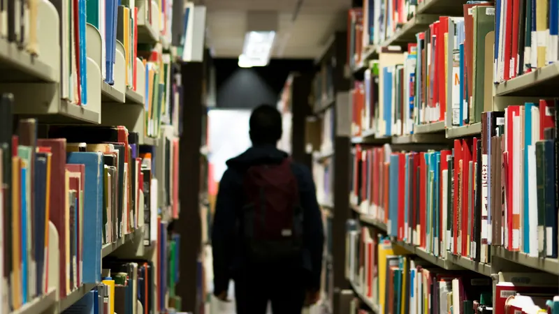 Person seen from behind walking between tall library bookshelves