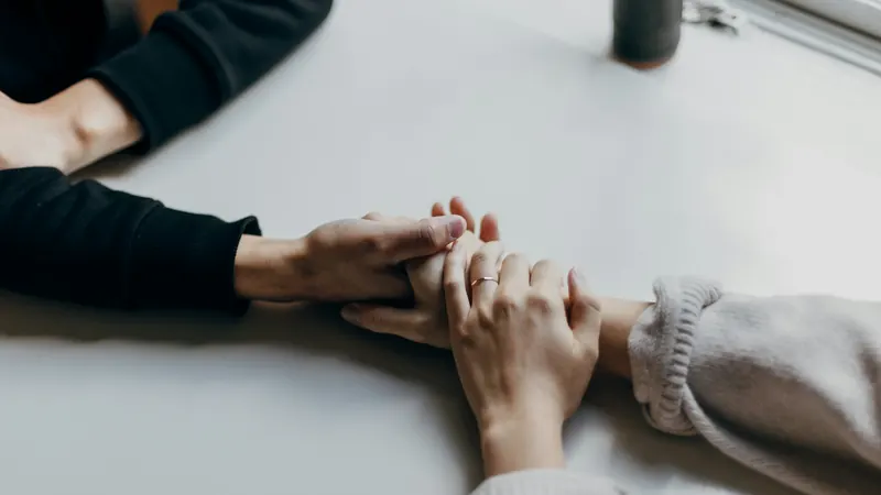 One person's hands gently holding another person's hands across a table