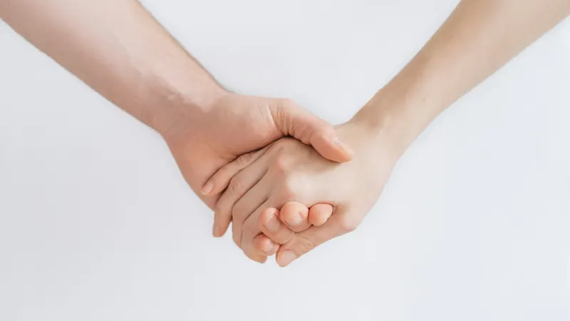 Two pairs of hands clasped together against a plain light background