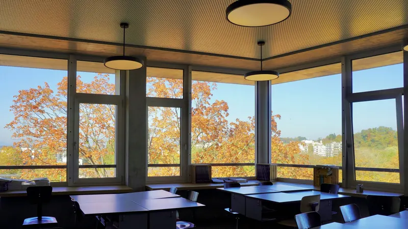 Classroom tables and chairs beside windows overlooking trees in autumn