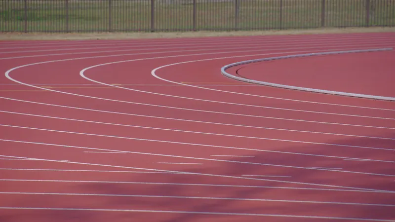 Empty red running track with curved white lane markings and fencing