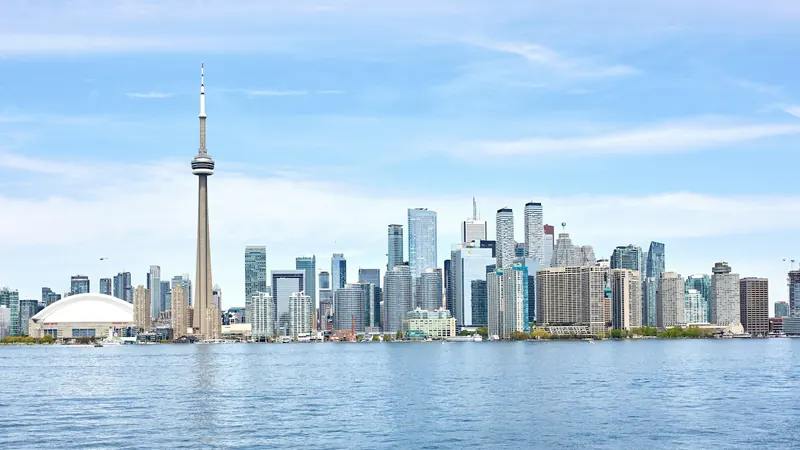Toronto waterfront skyline across blue water beneath a pale sky