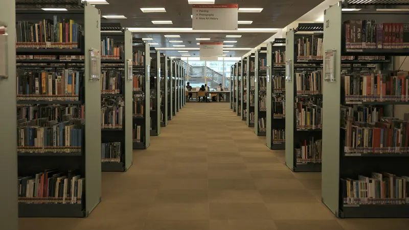 Rows of library bookshelves beneath ceiling lights on tiled floor