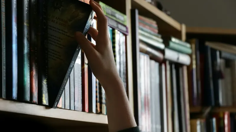 Hand reaching toward books arranged along a wooden library shelf