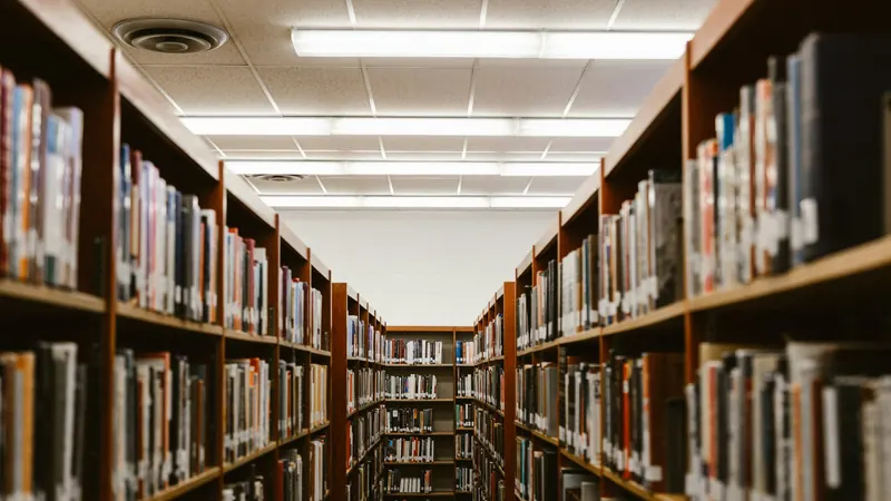 Library aisle with colourful books beneath rows of ceiling lights