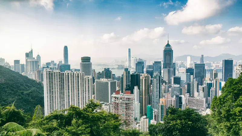 Hong Kong towers beyond green trees beneath a partly cloudy sky
