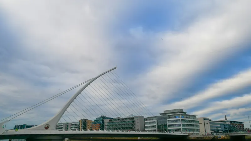 Curved white bridge support and cables beneath a cloudy sky
