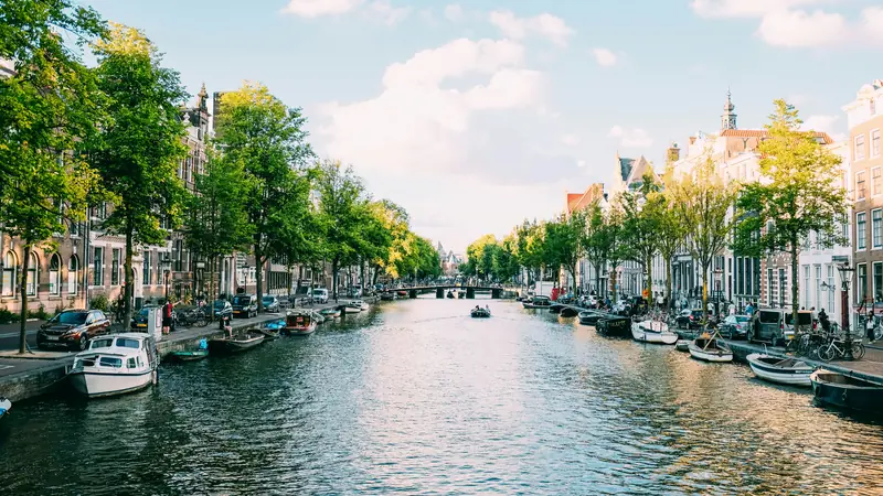 Tree lined canal with moored boats beside historic waterfront buildings