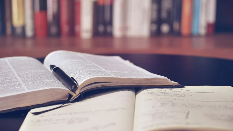 Open book and pen beside handwritten notes on a wooden table