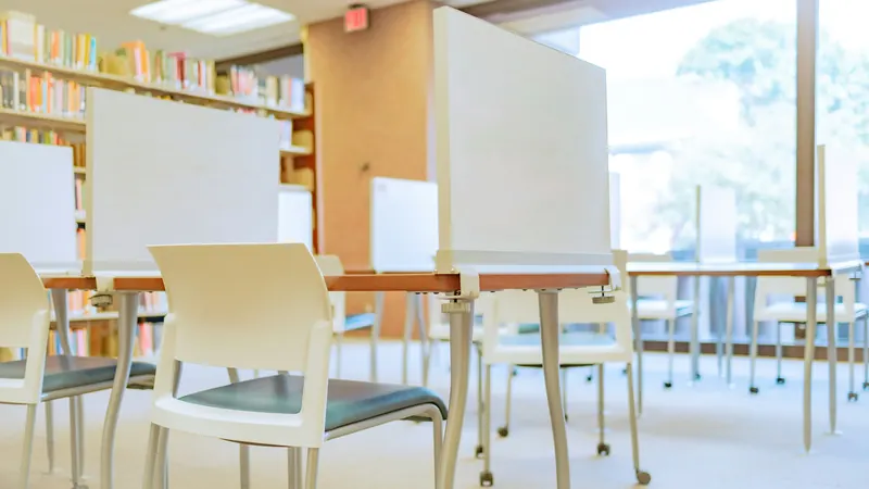 Empty chairs and study tables beside bookshelves in a bright library