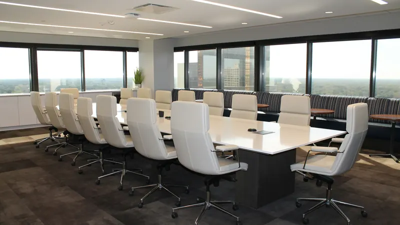 Long conference table surrounded by white chairs beside broad windows
